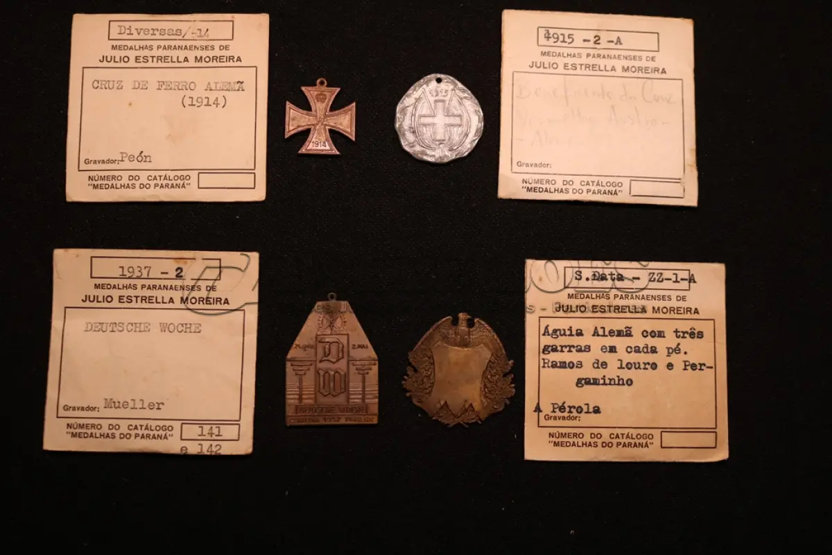 LOTE 036 - LOTE 36 – MEDALHAS ALEMANHA 	MEDALHA	OBSERVAÇÕES 1.		Cruz de Ferro Alemã. 1914 Gravador: José Peón	Reverso liso - envelope da Coleção Júlio Estrella Moreira 2.		Beneficente da Cruz Vermelha Austro-Alemã. 1915	Prateada - envelope da Coleção Júlio Estrella Moreira 3.		Deustche Woche (Semana Alemã). 1937. Curitiba Gravador: Eduardo Muller	Reverso liso - envelope da Coleção Júlio Estrella Moreira 4.		Águia Alemã com pergaminho Gravador: Henrique Kaminski – A Pérola	Reverso liso - envelope da Coleção Júlio Estrella Moreira