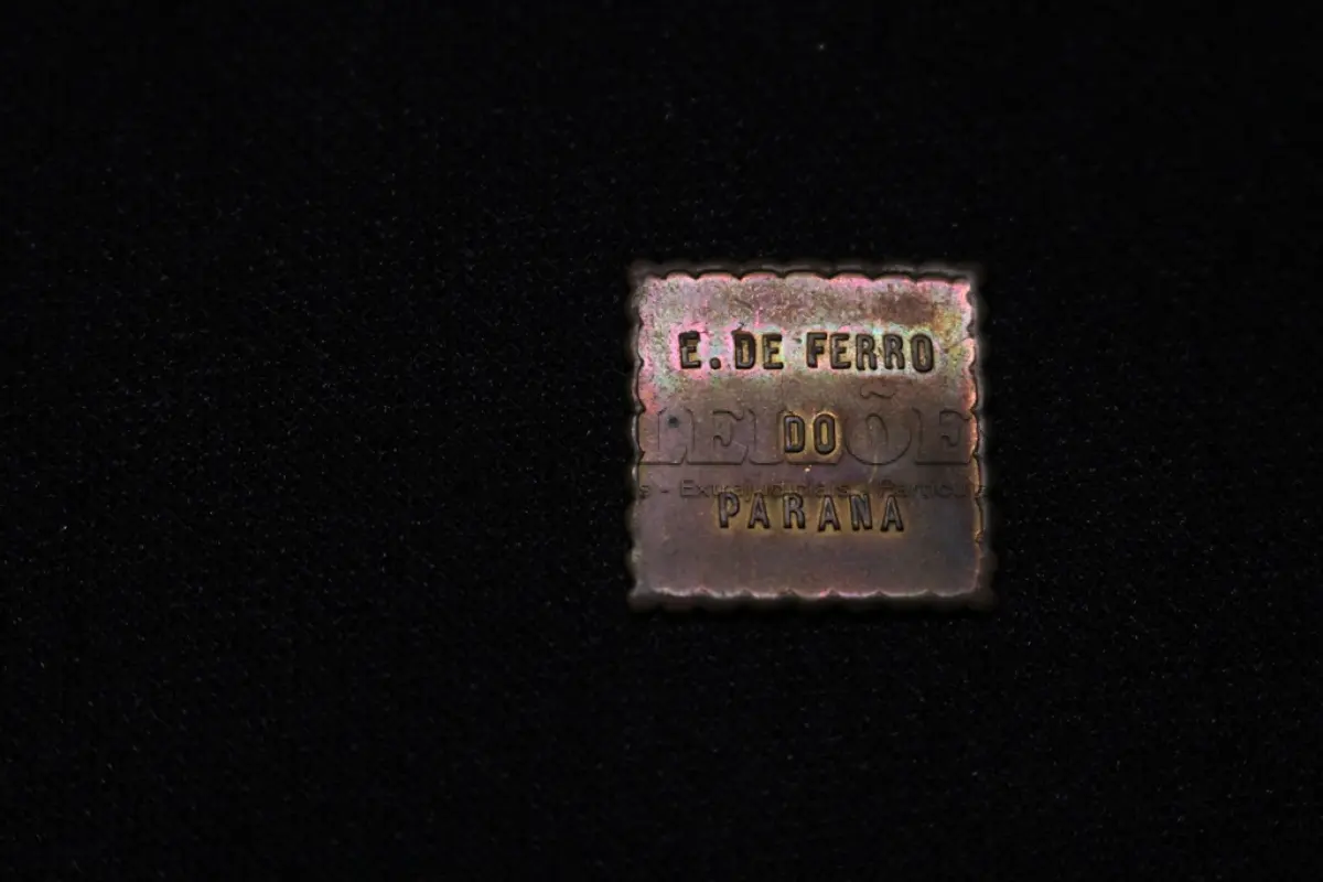 LOTE 038 - LOTE 38 – OBJETOS PECUNIÁRIOS CERÂMICA E FERROVIA ●	Fichas em cobre e alumínio, circulares; tendo na face o valor, no anverso, centralizado a figura de um pinheiro, dividindo ao as palavras MARCA REGIST, abaixo desta a inscrição CERAMICA DE PINHAES na orla, em circular com a inscrição "Pinhaes Paraná. Guilherme Weiss"  ●	Ficha de Fornecimento da Rede Ferroviária do Paraná 	OBJETO	OBSERVAÇÕES 1.		Ficha Cerâmica de Pinhaes - 100	Alumínio 2.		Ficha Cerâmica de Pinhaes - 100	Alumínio 3.		Ficha Cerâmica de Pinhaes - 100	Alumínio 4.		Ficha Cerâmica de Pinhaes - 100	Alumínio 5.		Ficha Cerâmica de Pinhaes - 100	Alumínio 6.		Ficha Cerâmica de Pinhaes - 200	Cobre 7.		Ficha de Fornecimentos da Rede Ferroviaria do PR - 50	Formato quadrado em metal estampado