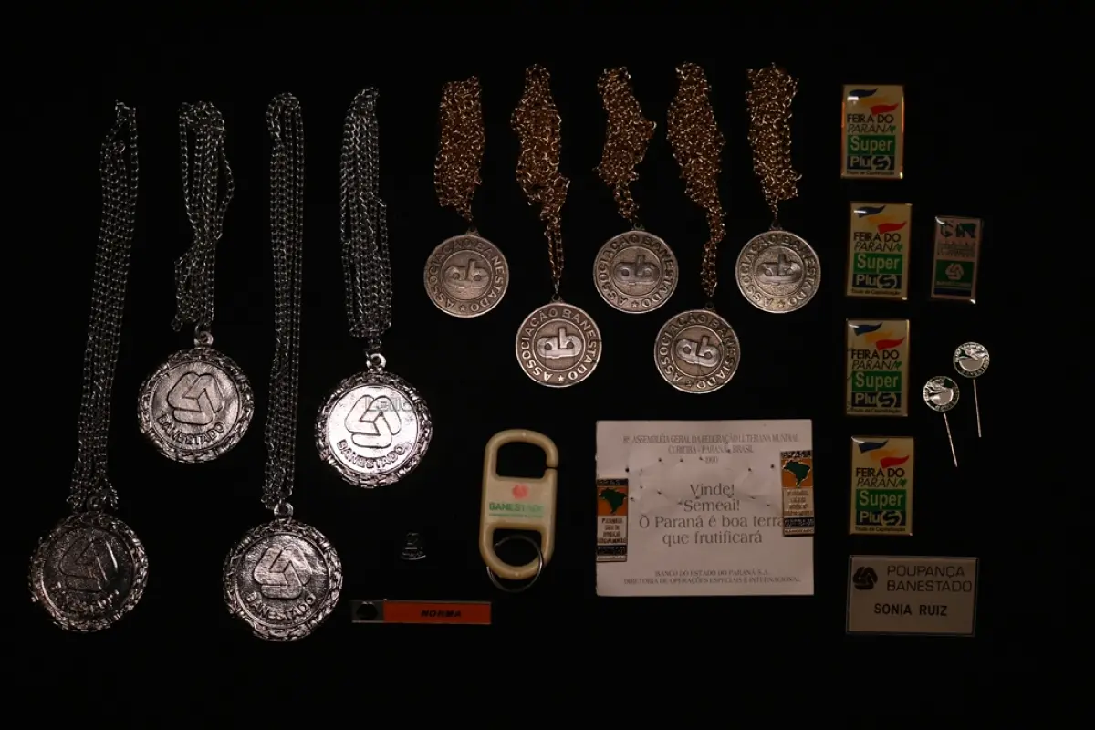 LOTE 047 - LOTE 47 – BANESTADO 	OBJETO	OBSERVAÇÕES 1.		Medalha Prateada Banestado – sem uso	4 unidades 2.		Medalha Associação Banestado – Inauguração Ginásio de Esportes-  30 de outubro de 1982	5 unidades 3.		Pin Banestado Feira do Paraná Super Plus Titulo de Capitalização.	4 unidades 4.		Pin CIN Centro Internacional de Negócios - Banestado	1 unidade 5.		Pin 8ª Assembleia Geral da Federação Luterana Mundial – 1998 - Banestado	2 unidades com encarte 6.		Crachá de funcionário Banestado em metal	1 unidade 7.		Crachá de funcionário Banestado em Acrílico	1 unidade 8.		Pin de lapela Banestado - integração	1 unidade 9.		Chaveiro Banestado de plástico branco	1 unidade 10.		Alfinete de Lapela Banestado – Pato Branco	2 unidades