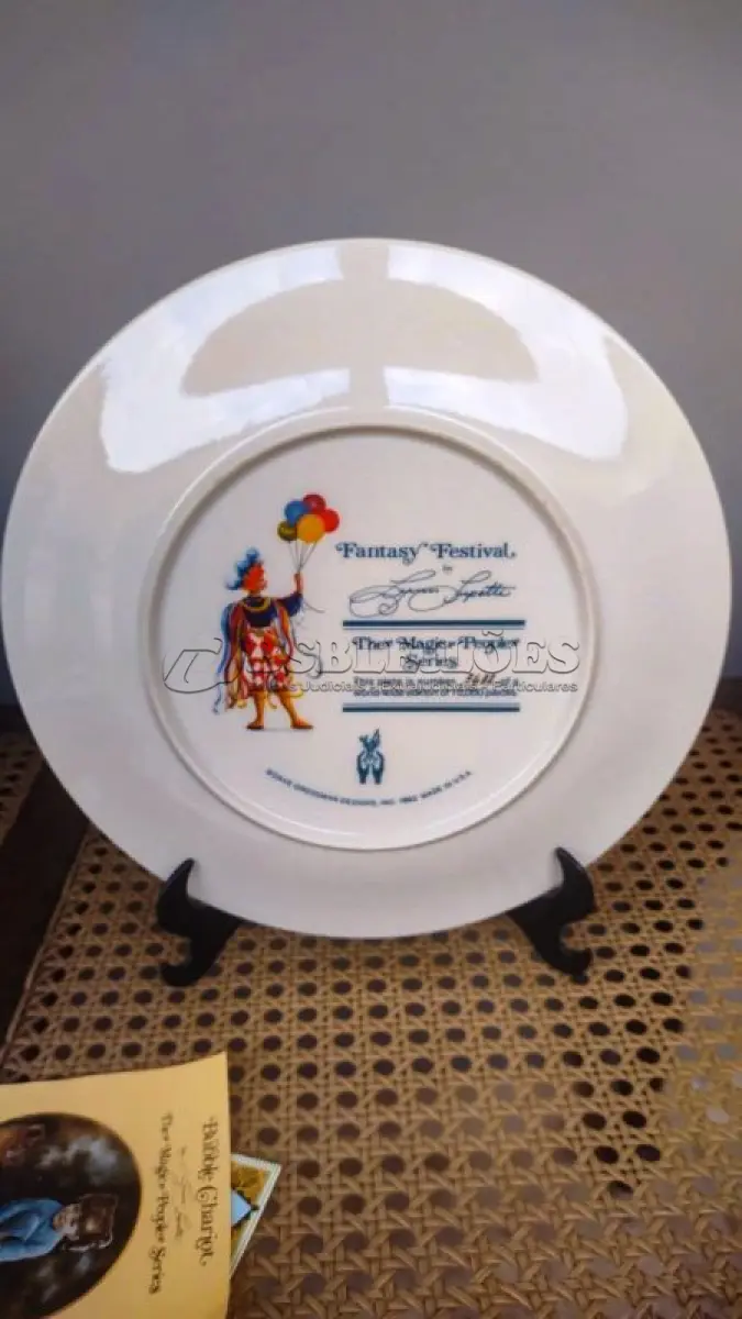 LOTE 238 - 01 RARO PRATO DE COLECIONADOR LYNN LUPETTI MAGIC PEOPLE FANTASY FESTIVAL É UMA ADIÇÃO VIBRANTE A QUALQUER COLEÇÃO, COM 26 CM DE DIÂMETRO. PRATO APRESENTA UM PADRÃO LÚDICO DE UM MENINO EM MEIO A UMA PAISAGEM MÁGICA E FANTÁSTICA, LINDAMENTE REPRESENTADO EM TONS DE AZUL E VERMELHO. CRIADO NOS ESTADOS UNIDOS EM 1982, ELE REMONTA AO FINAL DO SÉCULO XX, REFLETINDO A ARTE E O ESTILO DA DÉCADA DE 1980. FORAM LANÇADAS APENAS 10 MIL PEÇAS ESSE E O PRATO DE NUMERO 3638. UMA TÉCNICA DE PRODUÇÃO EM CERÂMICA ARTÍSTICA, ESTE ITEM DE COLECIONADOR FOI PROJETADO PARA SER EXIBIDO E APRECIADO EM TODAS AS OCASIÕES. O PRATO É UM TESTEMUNHO DA ESTÉTICA DA ÉPOCA, APRESENTANDO UM TEMA NOSTÁLGICO DE CRIANÇAS QUE CAPTURA A IMAGINAÇÃO E O ESPÍRITO DA ÉPOCA. SEJA VOCÊ UM COLECIONADOR EXPERIENTE OU SIMPLESMENTE UM APRECIADOR DO CHARME DE ITENS VINTAGE, ESTA PEÇA CERTAMENTE ENCANTARÁ.ITEM COMPRADO E GARAGENS DE ANTIGUIDADES NOS EUA.SUPORTE PARA PRATO NÃO INCLUÍDO NESTA VENDA. (NO ESTADO) ATENÇÃO! FAZER A VISITAÇÃO ANTES DE ARREMATAR, NÃO SABEMOS SE FUNCIONA, LEILÃO NÃO TEM GARANTIA E NEM DEVOLUÇÃO, SUJEITO A POSSÍVEIS AVARIAS VISÍVEIS/OCULTAS E/OU AUSÊNCIA DE COMPONENTES.
