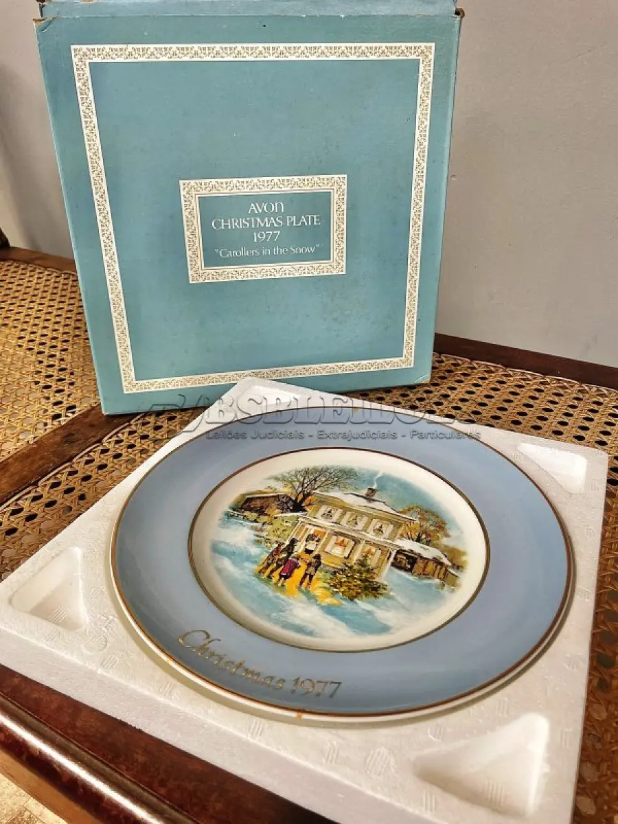 LOTE 030 - 01 LINDO PRATO DE NATAL DA SÉRIE AVON CHRISTMAS PLATE DE 1977, "CAROLLERS IN THE SNOW" - QUINTA EDIÇÃO DA SÉRIE. COM 22 CM DE DIÂMETRO E RETRATA UM GRUPO DE CANTORES DE NATAL EM FRENTE A UMA CASA DE DOIS ANDARES NO CENTRO. O VERSO MARCADO: SÉRIE DE PRATOS DE NATAL QUINTA EDIÇÃO "CANTORES DE NATAL NA NEVE" COM DOIS ANÉIS DE OURO 22K E O NATAL DE 1979 TAMBÉM EM OURO 22K.  FEITO EXCLUSIVAMENTE PARA A AVON CTS INC., 1977 POR ENOCH WEDGWOOD (TUNSTALL) LTD., INGLATERRA PEÇA COMPRADA EM GARAGEM DE ANTIGUIDADES NOS EUA. SUPORTE PARA PRATO NÃO INCLUÍDO NESTA VENDA. (NO ESTADO) ATENÇÃO! FAZER A VISITAÇÃO ANTES DE ARREMATAR, NÃO SABEMOS SE FUNCIONA, LEILÃO NÃO TEM GARANTIA E NEM DEVOLUÇÃO, SUJEITO A POSSÍVEIS AVARIAS VISÍVEIS/OCULTAS E/OU AUSÊNCIA DE COMPONENTES.