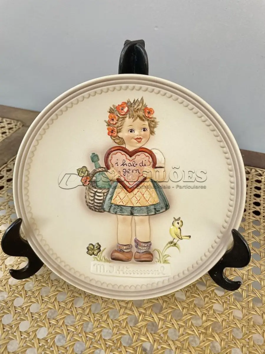 LOTE 060 - 01 RARO PRATO DE PORCELANA LINDAMENTE TRABALHADO DA FAMOSA M.J. HUMMEL GOEBEL APRESENTA UM FORMATO REDONDO E DESIGN MULTICOLORIDO, PERFEITO PARA TODAS AS OCASIÕES E ESTILOS DE DECORAÇÃO. É UM ITEM DE COLECIONADOR DA PRIMEIRA  EDIÇÃO DO PRATO VALENTINE GIFT, GRAVADO COM DETALHES INTRINCADOS E FABRICADO NA ALEMANHA NA DÉCADA DE 1980.PEÇA ÚNICA DA CULTURA ALEMÃ E VEM DA FRANQUIA GOEBEL, UMA MARCA RENOMADA NO SETOR DE COLECIONÁVEIS DECORATIVOS. LANÇADA SOMENTE PARA MEMBROS DO CLUBE DE COLECIONADORES GOEBEL. ITEM COMPRADO EM GARAGENS DE ANTIGUIDADES NOS EUA. OS ORIGINAIS OS PREÇO EM OUTROS PAÍSES  E DE 200 A 500 DÓLARES POR PEÇA VEJA NA FOTO .SUPORTE PARA PRATO NÃO INCLUÍDO NESTA VENDA. (NO ESTADO) ATENÇÃO! FAZER A VISITAÇÃO ANTES DE ARREMATAR, NÃO SABEMOS SE FUNCIONA, LEILÃO NÃO TEM GARANTIA E NEM DEVOLUÇÃO, SUJEITO A POSSÍVEIS AVARIAS VISÍVEIS/OCULTAS E/OU AUSÊNCIA DE COMPONENTES.