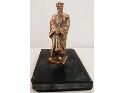 LOTE 081 - ESCULTURA  MAGISTRADO ALT.: 11 CM, BASE DE PEDRA FORMA DE LIVRO, DIM.: 2X9X12,5 CM  EM BRONZE MACIÇO (NO ESTADO)