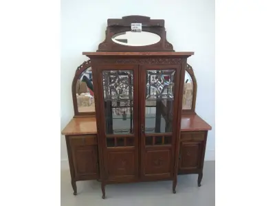 LOTE 040 - 01 CRISTALEIRA ANTIGA IMBUIA COM DETALHES ENTALHADOS NAS PORTAS, ESPELHOS LATERAIS, COM PORTA ENVIDRAÇADA EM CRISTAL BISOTADO. (NO ESTADO DE CONSERVAÇÃO QUE SE ENCONTRA) 