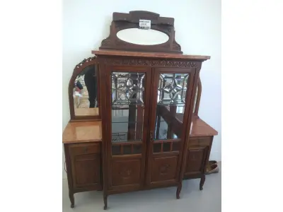 LOTE 040 - 01 CRISTALEIRA ANTIGA IMBUIA COM DETALHES ENTALHADOS NAS PORTAS, ESPELHOS LATERAIS, COM PORTA ENVIDRAÇADA EM CRISTAL BISOTADO. (NO ESTADO DE CONSERVAÇÃO QUE SE ENCONTRA) 