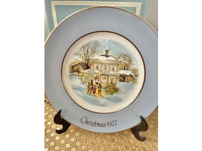 LOTE 030 - 01 LINDO PRATO DE NATAL DA SÉRIE AVON CHRISTMAS PLATE DE 1977, "CAROLLERS IN THE SNOW" - QUINTA EDIÇÃO DA SÉRIE. COM 22 CM DE DIÂMETRO E RETRATA UM GRUPO DE CANTORES DE NATAL EM FRENTE A UMA CASA DE DOIS ANDARES NO CENTRO. O VERSO MARCADO: SÉRIE DE PRATOS DE NATAL QUINTA EDIÇÃO "CANTORES DE NATAL NA NEVE" COM DOIS ANÉIS DE OURO 22K E O NATAL DE 1979 TAMBÉM EM OURO 22K.  FEITO EXCLUSIVAMENTE PARA A AVON CTS INC., 1977 POR ENOCH WEDGWOOD (TUNSTALL) LTD., INGLATERRA PEÇA COMPRADA EM GARAGEM DE ANTIGUIDADES NOS EUA. SUPORTE PARA PRATO NÃO INCLUÍDO NESTA VENDA. (NO ESTADO) ATENÇÃO! FAZER A VISITAÇÃO ANTES DE ARREMATAR, NÃO SABEMOS SE FUNCIONA, LEILÃO NÃO TEM GARANTIA E NEM DEVOLUÇÃO, SUJEITO A POSSÍVEIS AVARIAS VISÍVEIS/OCULTAS E/OU AUSÊNCIA DE COMPONENTES.