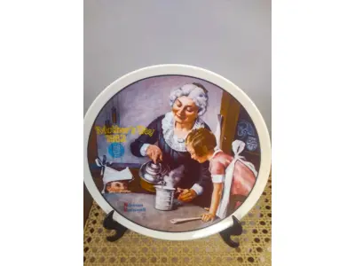 LOTE 179 - 01 PRATO DE NORMAN ROCKWELL PARA O DIA DAS MÃES DE 1982, "THE COOKING LESSON", DA PORCELANA FINA KNOWLES. O NÚMERO DO PRATO É 13025N , DA PRIMEIRA EDIÇÃO LIMITADA. O SÉTIMO DE UMA SÉRIE ANUAL PARA O DIA DAS MÃES. CERTIFICADO PELA ROCKWELL SOCIETY OF AMERICA. ESTE PRATO É UMA EDIÇÃO LIMITADA, PERMANENTEMENTE FECHADA, FEITA EM 7 DE MAIO DE 1982 PELA KNOWLES, A MARCA MAIS ANTIGA DA AMÉRICA EM PORCELANA FINA. O PRATO MEDE 21,8 CM DE DIÂMETRO E ESTÁ EM ÓTIMO ESTADO ITEM COMPRADO EM 2/10/1982 COM CERTIFICADO DE AUTENTICIDADE NOTAS E DOCUMENTOS DE COMPRA.  ITEM COMPRADO EM GARAGENS DE ANTIGUIDADES NOS EUA.SUPORTE PARA PRATO NÃO INCLUÍDO NESTA VENDA. (NO ESTADO) ATENÇÃO! FAZER A VISITAÇÃO ANTES DE ARREMATAR, NÃO SABEMOS SE FUNCIONA, LEILÃO NÃO TEM GARANTIA E NEM DEVOLUÇÃO, SUJEITO A POSSÍVEIS AVARIAS VISÍVEIS/OCULTAS E/OU AUSÊNCIA DE COMPONENTES.