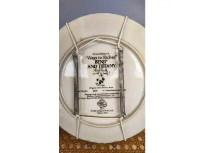 LOTE 328 - 01 PRATO BENJI E TIFFANY É O NÚMERO 2 DE UMA SÉRIE DE PRATOS INTITULADA "WAGS TO RICHES" DA CREATIVE WORLD. COM 21,8 CM DE DIÂMETRO E É LIMITADO A 19.500 PRATOS DO ARTISTA MURRAY KARN, ESTE E O PRATO DE NUMERO 844,1982. E PRODUZIDO PELA ROYAL MANOR PORCELAIN, É A 2ª EDIÇÃO DA COLEÇÃO WAGS TO RICHES.O PRATO ESTÁ EM EXCELENTE ESTADO. COM CERTIFICADO E CAIXA.PEÇA COMPRADA EM GARAGEM DE ANTIGUIDADES NOS EUA. “SUPORTE PARA PRATO NÃO INCLUÍDO NESTA VENDA.”