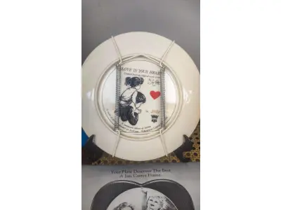 LOTE 139 - 01 LINDO PRATO DE COLECIONADOR DE SUE ETEM "LOVE IN YOUR HEART", ASSINADO À MÃO O PRATO TEM 21 CM É O Nº 5421 DE UMA EDIÇÃO LIMITADA DE 40.000 EXEMPLARES NO TOTAL DA AMERICAN LEGACY LTD. 1984 E RETRATA DUAS CRIANÇAS SE ABRAÇANDO. SUE ETEM É CONHECIDA POR SUAS BELAS REPRESENTAÇÕES DE CRIANÇAS EM CORES VIBRANTES E DIMENSÕES, E O PRATO É ASSINADO POR ELA NO VERSO, EM SUA CAIXA ORIGINAL. PEÇA COMPRADA EM GARAGEM DE ANTIGUIDADES NOS EUA. SUPORTE PARA PRATO NÃO INCLUÍDO NESTA VENDA. (NO ESTADO) ATENÇÃO! FAZER A VISITAÇÃO ANTES DE ARREMATAR, NÃO SABEMOS SE FUNCIONA, LEILÃO NÃO TEM GARANTIA E NEM DEVOLUÇÃO, SUJEITO A POSSÍVEIS AVARIAS VISÍVEIS/OCULTAS E/OU AUSÊNCIA DE COMPONENTES.