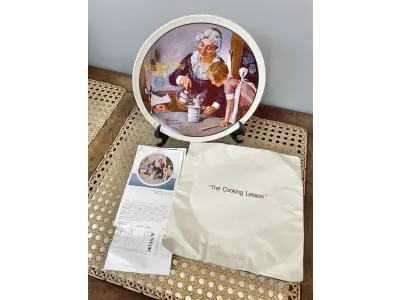 LOTE 161 - 01 PRATO DE NORMAN ROCKWELL PARA O DIA DAS MÃES DE 1982, "THE COOKING LESSON", DA PORCELANA FINA KNOWLES. O NÚMERO DO PRATO É 13025N , DA PRIMEIRA EDIÇÃO LIMITADA. O SÉTIMO DE UMA SÉRIE ANUAL PARA O DIA DAS MÃES. CERTIFICADO PELA ROCKWELL SOCIETY OF AMERICA. ESTE PRATO É UMA EDIÇÃO LIMITADA, PERMANENTEMENTE FECHADA, FEITA EM 7 DE MAIO DE 1982 PELA KNOWLES, A MARCA MAIS ANTIGA DA AMÉRICA EM PORCELANA FINA. O PRATO MEDE 21,8 CM DE DIÂMETRO E ESTÁ EM ÓTIMO ESTADO ITEM COMPRADO EM 2/10/1982 COM CERTIFICADO DE AUTENTICIDADE NOTAS E DOCUMENTOS DE COMPRA.  ITEM COMPRADO EM GARAGENS DE ANTIGUIDADES NOS EUA.SUPORTE PARA PRATO NÃO INCLUÍDO NESTA VENDA. (NO ESTADO) ATENÇÃO! FAZER A VISITAÇÃO ANTES DE ARREMATAR, NÃO SABEMOS SE FUNCIONA, LEILÃO NÃO TEM GARANTIA E NEM DEVOLUÇÃO, SUJEITO A POSSÍVEIS AVARIAS VISÍVEIS/OCULTAS E/OU AUSÊNCIA DE COMPONENTES.