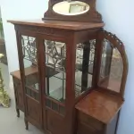 LOTE 040 - 01 CRISTALEIRA ANTIGA IMBUIA COM DETALHES ENTALHADOS NAS PORTAS, ESPELHOS LATERAIS, COM PORTA ENVIDRAÇADA EM CRISTAL BISOTADO. (NO ESTADO DE CONSERVAÇÃO QUE SE ENCONTRA) 