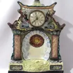 LOTE 034 - ANTIGO RELÓGIO IMPORTADO DA MARCA RUBINICH CONFECCIONADO EM FAIANÇA COM ESMALTAGEM BRANCA VITRIFICADA, CHINES  50 CM DE ALTURA X 37 CM DE LARGURA.(NO ESTADO)