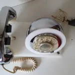 LOTE 084 - RARO TELEFONE ANOS 70. EM PLÁSTICO CROMADO E MECANISMO EM CAIXA DE ACRÍLICO MEDIDAS 24 CM COMP X 14,5 CM LARG X 19 CM ALT (NO ESTADO)