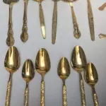 LOTE 117 - FAQUEIRO DOURADO PEÇAS: 6 TALHARES DE SERVIÇO, 12 COLHERES DE CHÁ, 5 COLHERES DE SOBREMESA, 2 GARFOS DE SOBREMESA, 9 GARFOS DE MESA, 5 COLHERES DE SOPA E 5 FACAS DE MESA.  44 PEÇAS (NO ESTADO)