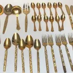 LOTE 117 - FAQUEIRO DOURADO PEÇAS: 6 TALHARES DE SERVIÇO, 12 COLHERES DE CHÁ, 5 COLHERES DE SOBREMESA, 2 GARFOS DE SOBREMESA, 9 GARFOS DE MESA, 5 COLHERES DE SOPA E 5 FACAS DE MESA.  44 PEÇAS (NO ESTADO)