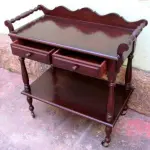LOTE 114 - RARO E LINDO CARRINHO DE CHÁ, MADEIRA MACIÇA, TORNEADAS, PRATELEIRA,  DUAS GAVETAS ALT:80 CM; LARG: 80 CM; PROF: 41 CM.(NO ESTADO)