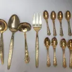 LOTE 117 - FAQUEIRO DOURADO PEÇAS: 6 TALHARES DE SERVIÇO, 12 COLHERES DE CHÁ, 5 COLHERES DE SOBREMESA, 2 GARFOS DE SOBREMESA, 9 GARFOS DE MESA, 5 COLHERES DE SOPA E 5 FACAS DE MESA.  44 PEÇAS (NO ESTADO)