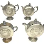 LOTE 175 - RARO JOGO DE CHÁ E CAFÉ EM METAL, REDONDO, COM DECORAÇÃO EM ALTO RELEVO, SENDO DOIS BOWLS (23 X 23 E 21 X 23 CM), LEITEIRA (18,5 X 20 CM) E AÇUCAREIRO (17,5 X 17 CM - MOSSA). (NO ESTADO)