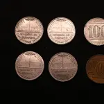 LOTE 038 - LOTE 38 – OBJETOS PECUNIÁRIOS CERÂMICA E FERROVIA ●	Fichas em cobre e alumínio, circulares; tendo na face o valor, no anverso, centralizado a figura de um pinheiro, dividindo ao as palavras MARCA REGIST, abaixo desta a inscrição CERAMICA DE PINHAES na orla, em circular com a inscrição "Pinhaes Paraná. Guilherme Weiss"  ●	Ficha de Fornecimento da Rede Ferroviária do Paraná 	OBJETO	OBSERVAÇÕES 1.		Ficha Cerâmica de Pinhaes - 100	Alumínio 2.		Ficha Cerâmica de Pinhaes - 100	Alumínio 3.		Ficha Cerâmica de Pinhaes - 100	Alumínio 4.		Ficha Cerâmica de Pinhaes - 100	Alumínio 5.		Ficha Cerâmica de Pinhaes - 100	Alumínio 6.		Ficha Cerâmica de Pinhaes - 200	Cobre 7.		Ficha de Fornecimentos da Rede Ferroviaria do PR - 50	Formato quadrado em metal estampado