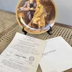 01 RARO PRATO DE NORMAN ROCKWELL "CONFIANDO NA TOCA" PEÇA DE COLECIONADOR VINTAGE NORMAN ROCKWELL " EM INGLÊS "CONFIDING IN THE DEN" COM DETALHES EM OURO 24K. PRATO NUMERADO DE PORCELANA FINA EDWIN M. KNOWLES. EDIÇÃO LIMITADA DE NORMAN ROCKWELL, DÉCIMA PRIMEIRA EDIÇÃO DA COLEÇÃO MULHERES REDESCOBERTAS DE ROCKWELL, FEITA EM UMA EDIÇÃO ESTRITAMENTE LIMITADA A CEM DIAS DE QUEIMA E CERTIFICADA COMO UM "VERDADEIRO CLÁSSICO ROCKWELL" PELA ROCKWELL SOCIETY OF AMERICA. COM CERTIFICADO DE AUTENTICIDADE E CAIXA ORIGINAL. O PRATO MEDE 21,5 CM DE DIÂMETRO. SUPORTE PARA PRATO NÃO INCLUÍDO NESTA VENDA. (NO ESTADO) ATENÇÃO! FAZER A VISITAÇÃO ANTES DE ARREMATAR, NÃO SABEMOS SE FUNCIONA, LEILÃO NÃO TEM GARANTIA E NEM DEVOLUÇÃO, SUJEITO A POSSÍVEIS AVARIAS VISÍVEIS/OCULTAS E/OU AUSÊNCIA DE COMPONENTES.