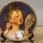 01 RARO PRATO PARA AMANTES E COLECIONADORES DE NORMAN ROCKWELL! ESTE É UM PRATO COLECIONÁVEL DE PORCELANA VINTAGE DE EDIÇÃO LIMITADA. "MAKING BELIEVE AT THE MIRROR" É A QUARTA PLACA DA COLEÇÃO DE EDIÇÃO LIMITADA INTITULADA ROCKWELL'S REDISCOVERED WOMEN, UMA SÉRIE QUE OFERECE UMA RETROSPECTIVA ÚNICA DAS OBRAS DE NORMAN ROCKWELL. ESTA OBRA É OFICIALMENTE CERTIFICADA PELA ROCKWELL SOCIETY OF AMERICA. FOI ENCONTRADA EM UM ARMÁRIO DURANTE A VENDA DE UMA PROPRIEDADE, APÓS MUITOS ANOS GUARDADA.  CAIXA ORIGINAL E CERTIFICADO DE AUTENTICIDADE DA PEÇA  O PRATO MEDE 21,5 CM DE DIÂMETRO.  SUPORTE PARA PRATO NÃO INCLUÍDO NESTA VENDA. (NO ESTADO) ATENÇÃO! FAZER A VISITAÇÃO ANTES DE ARREMATAR, NÃO SABEMOS SE FUNCIONA, LEILÃO NÃO TEM GARANTIA E NEM DEVOLUÇÃO, SUJEITO A POSSÍVEIS AVARIAS VISÍVEIS/OCULTAS E/OU AUSÊNCIA DE COMPONENTES.