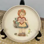 01 RARO PRATO DE PORCELANA LINDAMENTE TRABALHADO DA FAMOSA M.J. HUMMEL GOEBEL APRESENTA UM FORMATO REDONDO E DESIGN MULTICOLORIDO, PERFEITO PARA TODAS AS OCASIÕES E ESTILOS DE DECORAÇÃO. É UM ITEM DE COLECIONADOR DA PRIMEIRA  EDIÇÃO DO PRATO VALENTINE GIFT, GRAVADO COM DETALHES INTRINCADOS E FABRICADO NA ALEMANHA NA DÉCADA DE 1980.PEÇA ÚNICA DA CULTURA ALEMÃ E VEM DA FRANQUIA GOEBEL, UMA MARCA RENOMADA NO SETOR DE COLECIONÁVEIS DECORATIVOS. LANÇADA SOMENTE PARA MEMBROS DO CLUBE DE COLECIONADORES GOEBEL. ITEM COMPRADO EM GARAGENS DE ANTIGUIDADES NOS EUA. OS ORIGINAIS OS PREÇO EM OUTROS PAÍSES  E DE 200 A 500 DÓLARES POR PEÇA VEJA NA FOTO .SUPORTE PARA PRATO NÃO INCLUÍDO NESTA VENDA. (NO ESTADO) ATENÇÃO! FAZER A VISITAÇÃO ANTES DE ARREMATAR, NÃO SABEMOS SE FUNCIONA, LEILÃO NÃO TEM GARANTIA E NEM DEVOLUÇÃO, SUJEITO A POSSÍVEIS AVARIAS VISÍVEIS/OCULTAS E/OU AUSÊNCIA DE COMPONENTES.