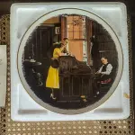 01 RARO E GRANDE PRATO ASSINADO POR NORMAN ROCKWELL, COM 26,50 CM DE DIÂMETRO EDIÇÃO LIMITADA, COM CERTIFICADO DE AUTENTICIDADE EM TONS QUENTES DE MARROM E AMARELO SUAVE, CAPTURA UM MOMENTO ATEMPORAL DE AMOR E COMPROMISSO. A CENA MOSTRA UM CASAL ELEGANTEMENTE VESTIDO ASSINANDO SUA CERTIDÃO DE CASAMENTO. UM CELEBRANTE, SENTADO PRÓXIMO, OBSERVA O MOMENTO COM UMA EXPRESSÃO GENTIL, ADICIONANDO UM TOQUE DE SERIEDADE E TRADIÇÃO À COMPOSIÇÃO. O PRATO  COM ELEGANTES DETALHES DOURADOS NAS BORDAS, REALÇANDO SEU TOQUE CLÁSSICO E SOFISTICADO.UMA BELA REPRESENTAÇÃO DA CAPACIDADE DE ROCKWELL DE CAPTURAR MOMENTOS ÍNTIMOS DA VIDA COM CHARME E DETALHES. ITEM COMPRADO EM GARAGEM DE ANTIGUIDADES NOS EUA.SUPORTE PARA PRATO NÃO INCLUÍDO NESTA VENDA.SUPORTE PARA PRATO NÃO INCLUÍDO NESTA VENDA. (NO ESTADO) ATENÇÃO! FAZER A VISITAÇÃO ANTES DE ARREMATAR, NÃO SABEMOS SE FUNCIONA, LEILÃO NÃO TEM GARANTIA E NEM DEVOLUÇÃO, SUJEITO A POSSÍVEIS AVARIAS VISÍVEIS/OCULTAS E/OU AUSÊNCIA DE COMPONENTES.